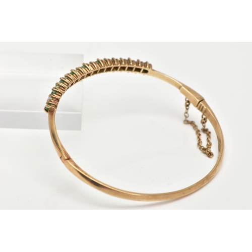 60 - A 9CT GOLD EMERALD AND OPAL BANGLE, hinged bangle, designed with a row of circular cut emeralds inte... 