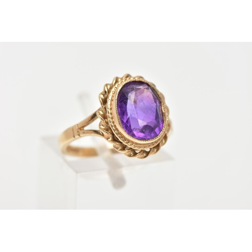 34 - A 9CT GOLD AMETHYST DRESS RING, an oval cut amethyst set in a yellow gold bezel setting and a rope t... 