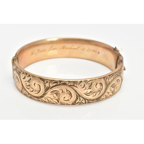 64 - A 9CT GOLD METAL CORE BANGLE, half with a foliate scroll detail, fitted with a push pin clasp, missi... 