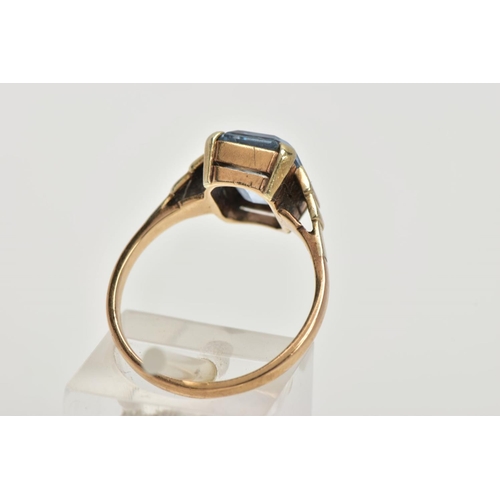 110 - A YELLOW METAL RING, designed with an emerald cut pale blue stone assessed as synthetic spinel, step... 