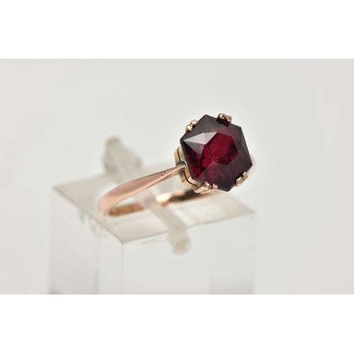 43 - A YELLOW METAL GARNET RING, designed with a double four claw set, hexagonal cut garnet, tapered shou... 