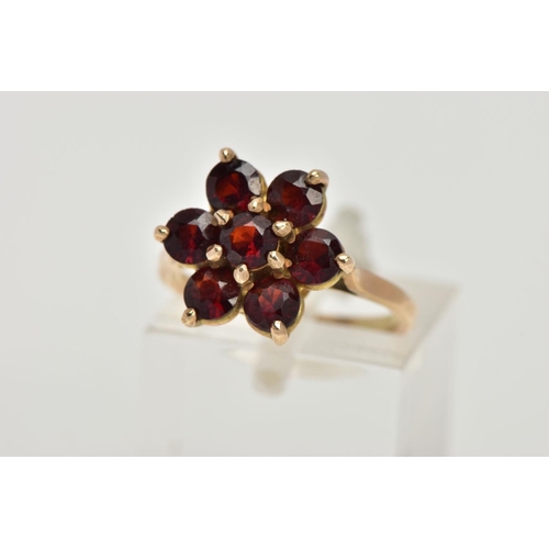 61 - A YELLOW METAL GARNET CLUSTER RING, in the form of a flower cluster, set with seven circular cut gar... 