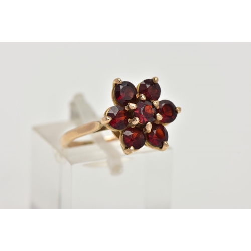 61 - A YELLOW METAL GARNET CLUSTER RING, in the form of a flower cluster, set with seven circular cut gar... 