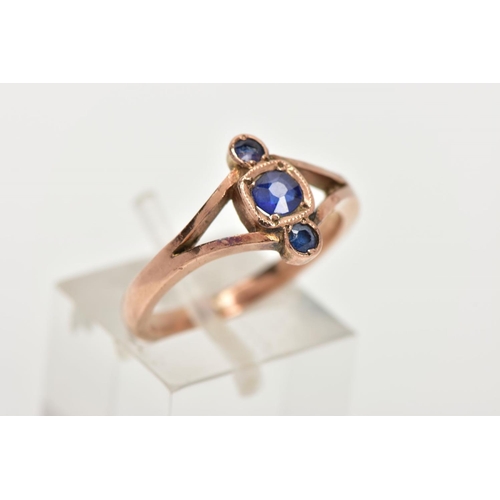 116 - A THREE STONE RING, three graduated circular cut blue stones, within a rose gold tone mount, bifurca... 