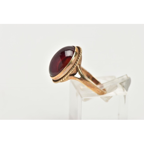 157 - A 9CT GOLD RING, designed with a hollowed out, oval red cabochon, bezel set with a rope twist surrou... 