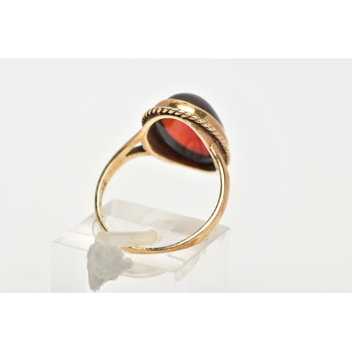 157 - A 9CT GOLD RING, designed with a hollowed out, oval red cabochon, bezel set with a rope twist surrou... 