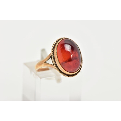 157 - A 9CT GOLD RING, designed with a hollowed out, oval red cabochon, bezel set with a rope twist surrou... 