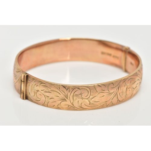 70 - A 9CT GOLD HINGED BANGLE, decorated with a foliate design all round, approximate band width 12.7mm, ... 