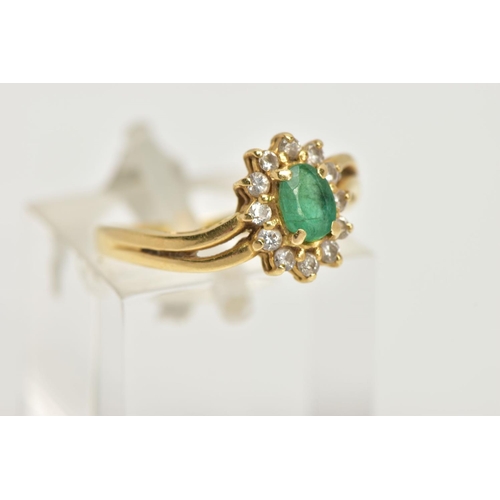 17 - A YELLOW METAL EMERALD AND DIAMOND RING, an oval cut emerald prong set within a surround of twelve r... 