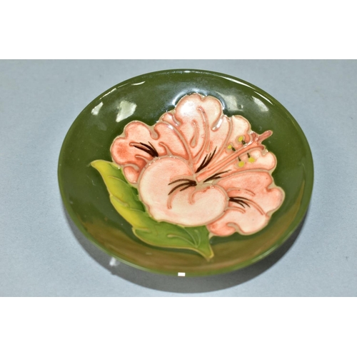 500 - A MOORCROFT POTTERY CIRCULAR PIN DISH DECORATED WITH CORAL HIBISCUS ON A GREEN GROUND, faint impress... 