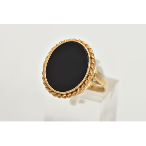 41 - A 9CT GOLD ONYX RING, a large oval onyx slice, inlayed in a yellow gold mount with a rope detail sur... 