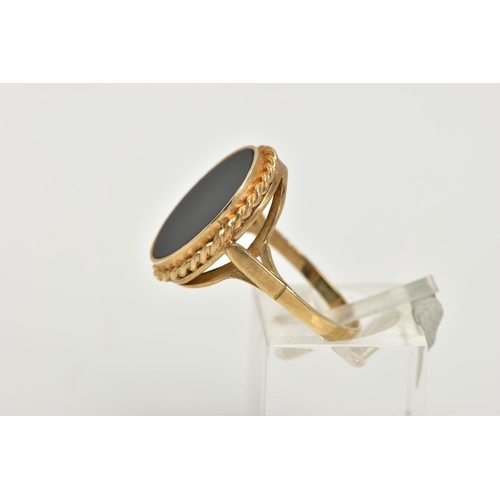 41 - A 9CT GOLD ONYX RING, a large oval onyx slice, inlayed in a yellow gold mount with a rope detail sur... 