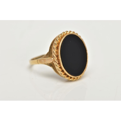 41 - A 9CT GOLD ONYX RING, a large oval onyx slice, inlayed in a yellow gold mount with a rope detail sur... 