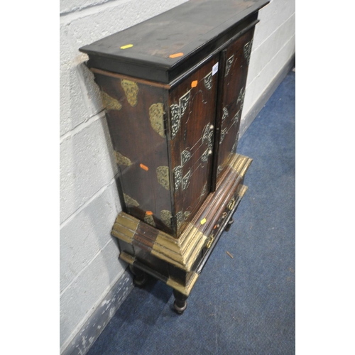 1652 - AN ANTIQUE HARDWOOD AND BRASS BANDED TWO DOOR CABINET, likely to be far Eastern, on a base with a si... 