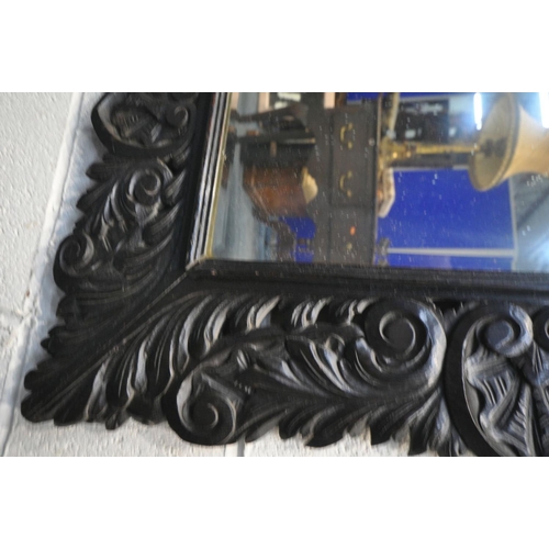 1658 - A 19TH CENTURY EBONISED CARVED OAK WALL MIRROR, with lions mask and foliate decoration, and bevelled... 