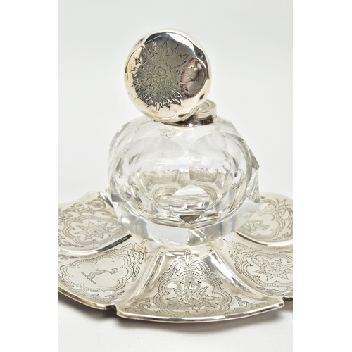 49 - A VICTORIAN SILVER AND GLASS INKWELL ON STAND, of wavy circular outline, foliate engraved decoration... 