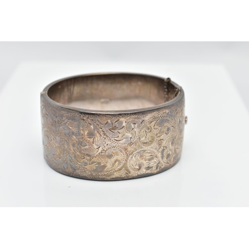 69 - A WIDE SILVER HINGED BANGLE, with a scrolling foliate design, fitted with a push button integrated b... 