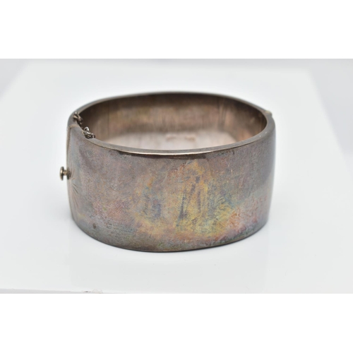 69 - A WIDE SILVER HINGED BANGLE, with a scrolling foliate design, fitted with a push button integrated b... 