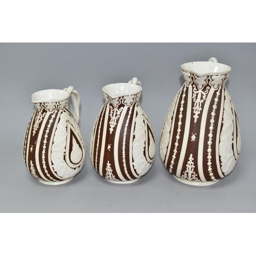 533 - THREE NINETEENTH CENTURY COBRIDGE CASHMERE GRADUATING JUGS, having cream on dark brown moulded folia... 