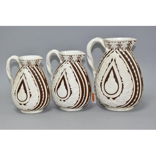 533 - THREE NINETEENTH CENTURY COBRIDGE CASHMERE GRADUATING JUGS, having cream on dark brown moulded folia... 