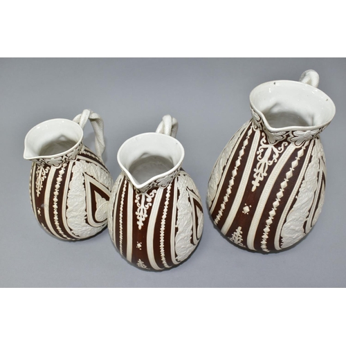 533 - THREE NINETEENTH CENTURY COBRIDGE CASHMERE GRADUATING JUGS, having cream on dark brown moulded folia... 