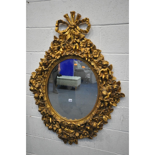 1334 - A 20TH CENTURY GILT OVAL WALL MIRROR, depicting a ribbon surmount, nine putto's with instruments, wi... 