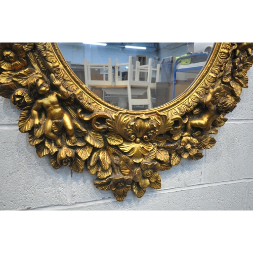 1334 - A 20TH CENTURY GILT OVAL WALL MIRROR, depicting a ribbon surmount, nine putto's with instruments, wi... 