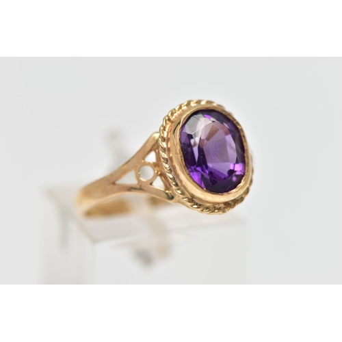 33 - A 9CT GOLD AMETHYST SINGLE STONE RING, the oval cut amethyst collet set, within a rope twist surroun... 