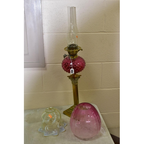 605 - A LATE VICTORIAN OIL LAMP, the acid etched cranberry glass shade with broken section, cranberry rese... 