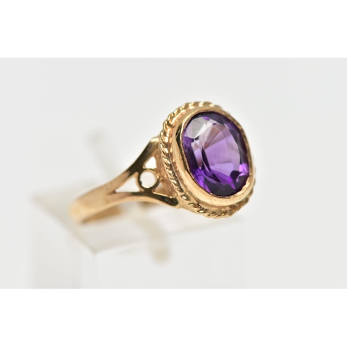 188 - A 9CT GOLD AMETHYST SINGLE STONE RING, the oval cut amethyst collet set, within a rope twist surroun... 