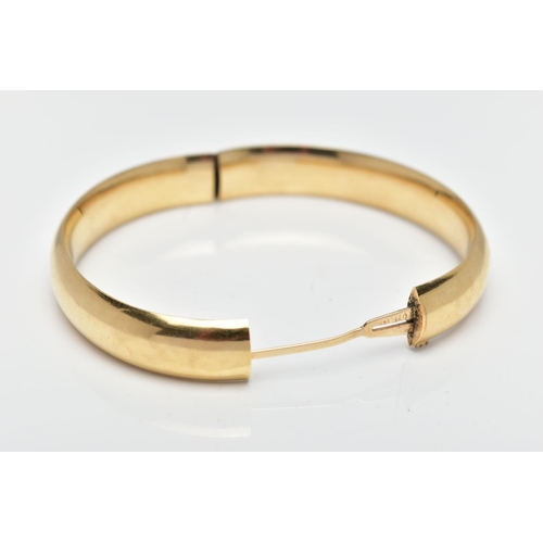 58 - A YELLOW METAL BANGLE, a polished hollow yellow metal oval hinged bangle, fitted with a push pin int... 