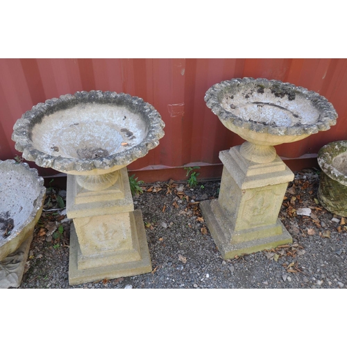 1007 - A PAIR OF MODRN COMPOSITE GARDEN URNS on square columns with pie crust top edges, baluster and flute... 