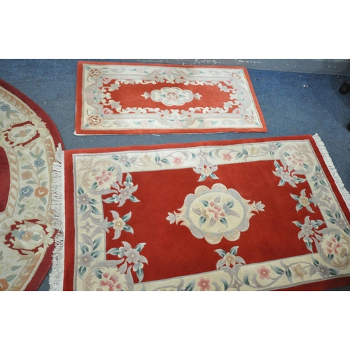 1260 - A RED GROUND CIRCULAR RUG, with cream border and centre, diameter 185cm, and two similar rectangular... 