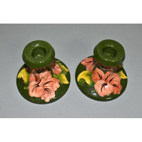 321 - A PAIR OF MOORCROFT POTTERY DWARF CANDLESTICKS, coral 'Hibiscus' pattern on green ground, partial im... 