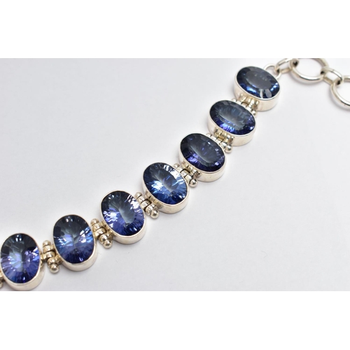 15 - A SILVER IOLITE BRACELET, the oval cut iolites collet set, with hinged spacers, to the circular link... 