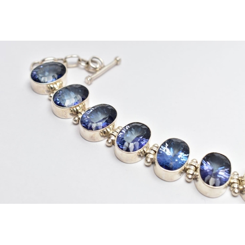 15 - A SILVER IOLITE BRACELET, the oval cut iolites collet set, with hinged spacers, to the circular link... 