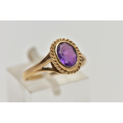 21 - A 9CT GOLD AMETHYST SINGLE STONE RING, the oval cut amethyst within a collet setting, to the openwor... 