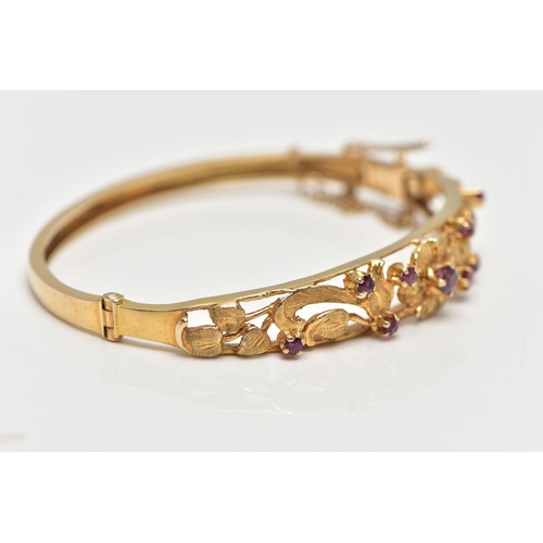 59 - A 9CT GOLD FLORAL BANGLE, a yellow gold oval form hinged bangle, open work textured detail set with ... 