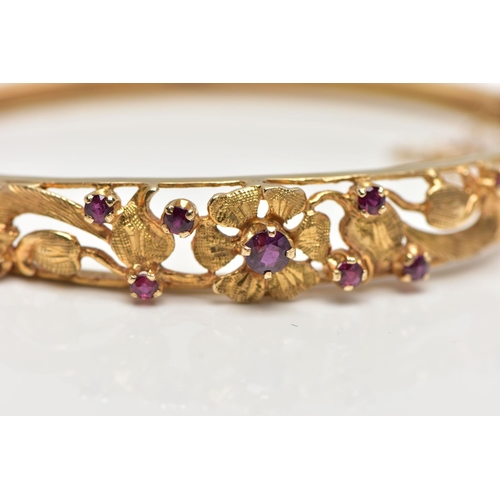 59 - A 9CT GOLD FLORAL BANGLE, a yellow gold oval form hinged bangle, open work textured detail set with ... 