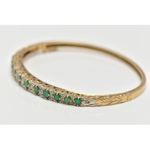 3 - A 9CT GOLD, EMERALD AND DIAMOND HINGED BANGLE, designed with a row of eleven, claw set, circular cut... 