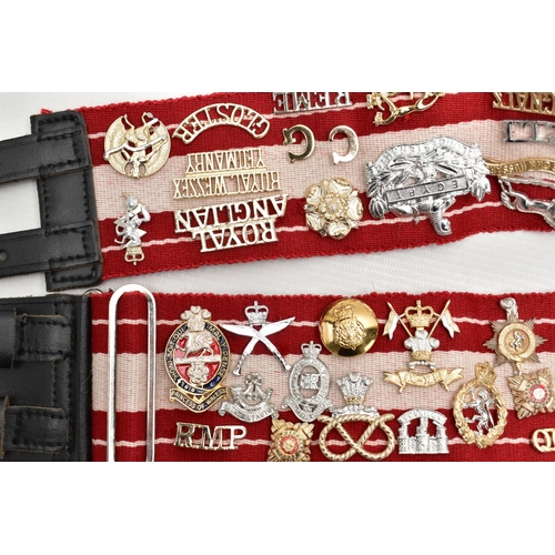 157 - A RED AND WHITE MILITARY STYLE STABLE BELT, which has had mounted over 45 Military Badges, Cap devic... 