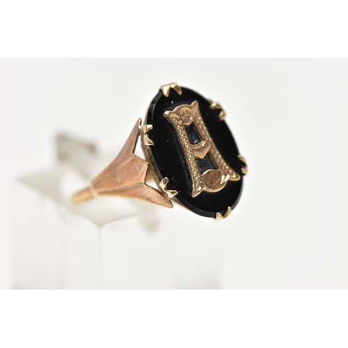 38 - A YELLOW METAL INITIAL RING, an oval cut onyx centrally set with a yellow metal letter, prong set in... 