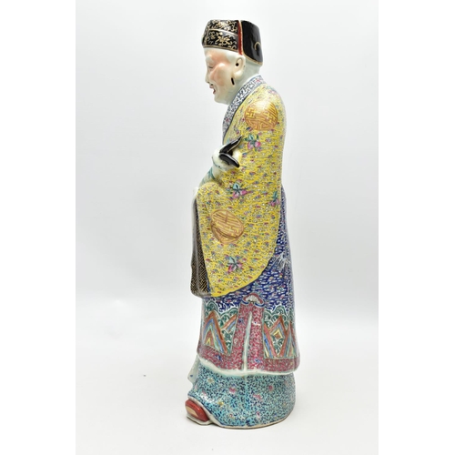 120 - A 20TH CENTURY CHINESE FAMILLE ROSE STANDING FIGURE, modelled as a male wearing flowing robes holdin... 