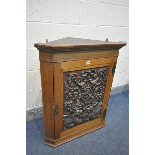 1304 - A 20TH CENTURY OAK HANDING CORNER CUPBOARD, with a heavily carved foliate panel, a depicting a centr... 