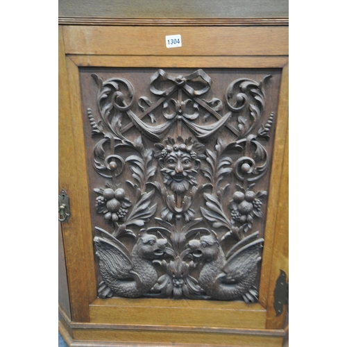 1304 - A 20TH CENTURY OAK HANDING CORNER CUPBOARD, with a heavily carved foliate panel, a depicting a centr... 