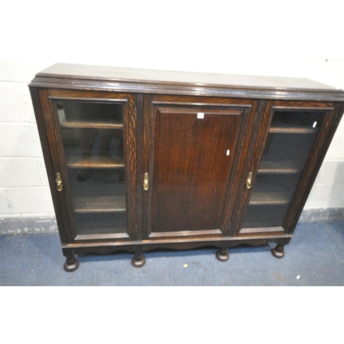 1352 - A 20TH CENTURY OAK BOOKCASE, with two glazed doors, flanking a single panelled door, enclosing adjus... 