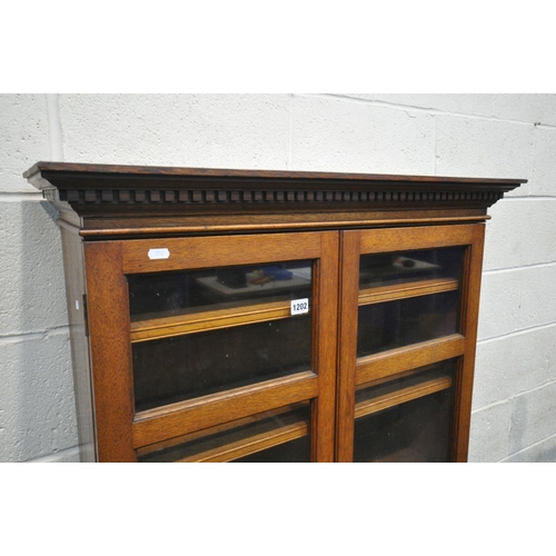 1202 - AN EARLY 20TH CENTURY OAK GLAZED TWO DOOR BOOKCASE, on square tapered legs, width 83cm x depth 31cm ... 