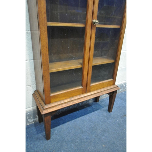 1202 - AN EARLY 20TH CENTURY OAK GLAZED TWO DOOR BOOKCASE, on square tapered legs, width 83cm x depth 31cm ... 