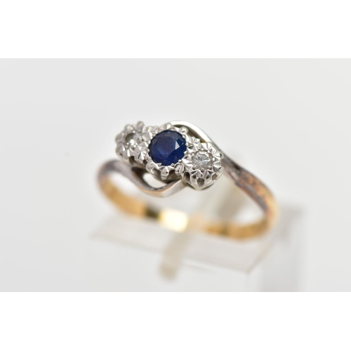 19 - A YELLOW METAL CROSS OVER THREE STONE RING, designed with a central circular cut blue sapphire, flan... 