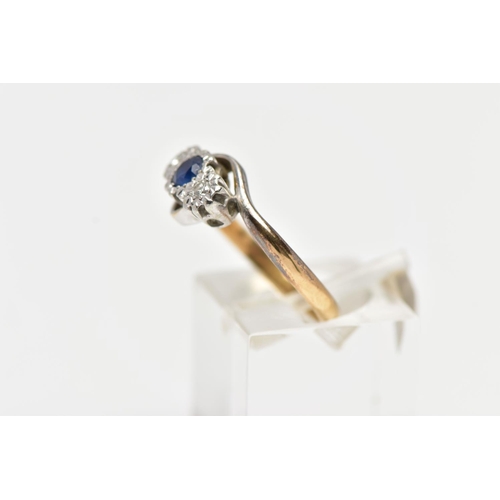 19 - A YELLOW METAL CROSS OVER THREE STONE RING, designed with a central circular cut blue sapphire, flan... 